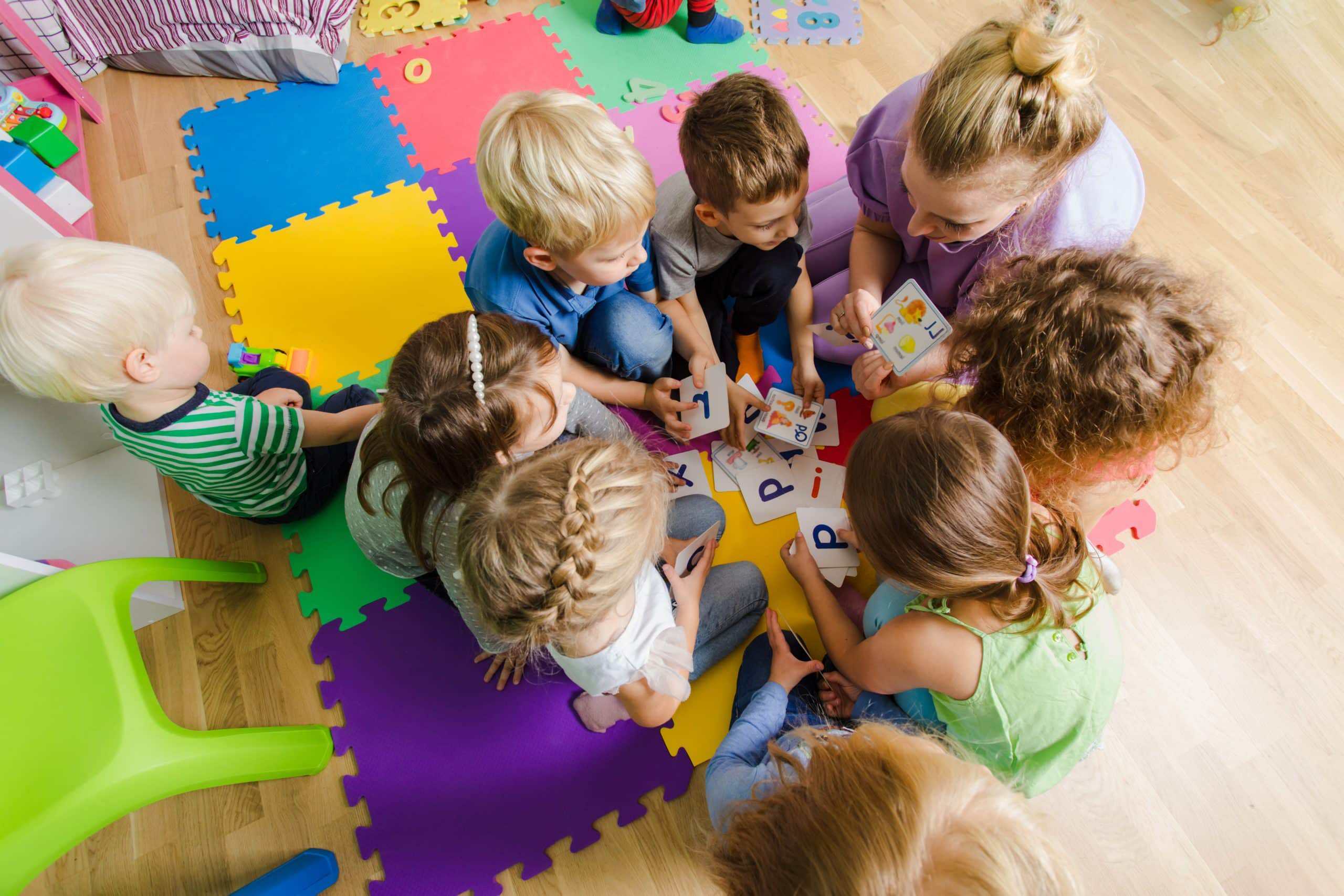 Group of kindergarten kids sitting closely on a floor together with teacher, providing group work. Children learning to cooperate while solving tasks.